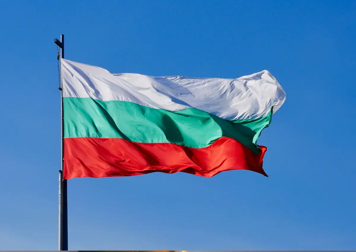 Die Nationalflagge von Bulgarien mit den horizontalen Streifen in Weiß, Grün und Rot weht an einem Mast vor strahlend blauem Himmel – Zur digitalen Vignette Bulgarien (BGTOLL) auf mautbox24.com.