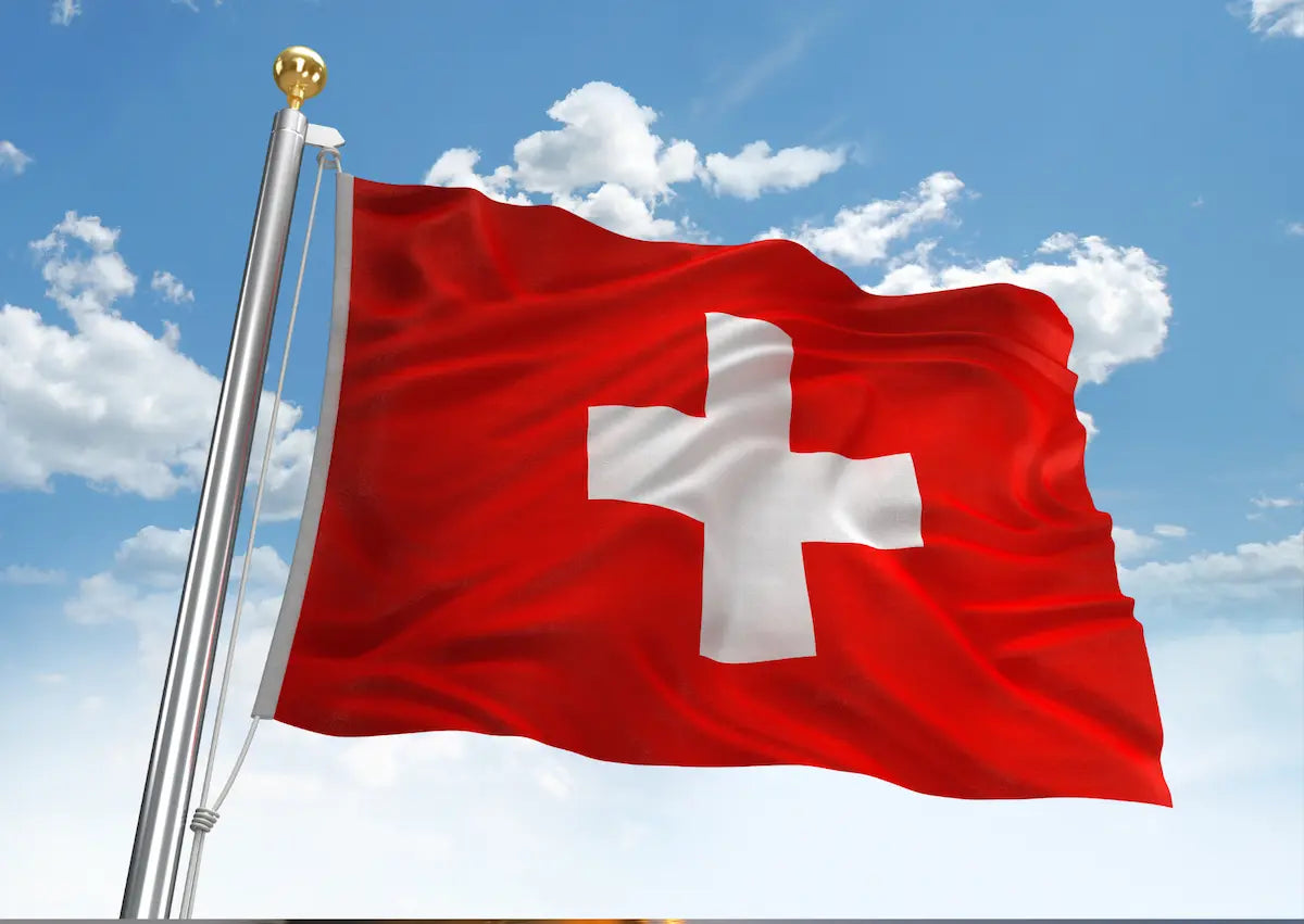 Die rote Schweizer Flagge mit dem weißen Kreuz weht im Wind vor blauem Himmel – Zur digitalen Vignette Schweiz (E-Vignette) auf mautbox24.com.